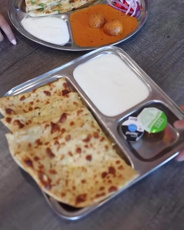 Naan, curry, raita and salad served on steel trays