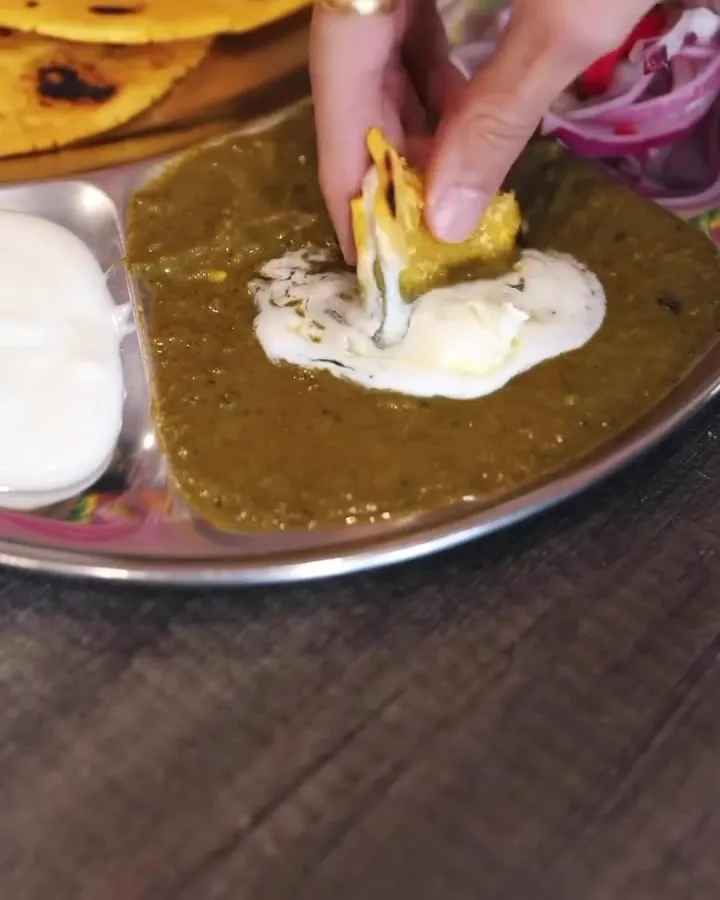 Makki roti dipped into saag, with yogurt on the side